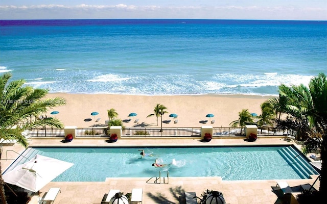 view of pool featuring a water view, a patio area, and a view of the beach