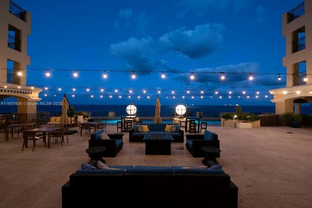 patio at night featuring a community pool, a water view, and an outdoor living space with a fire pit