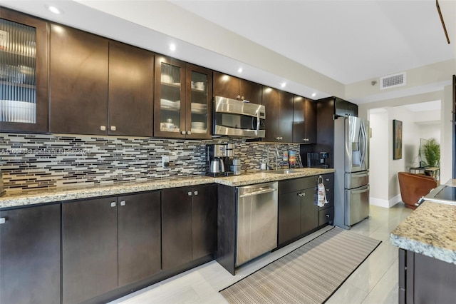 kitchen featuring dark brown cabinetry, light stone countertops, and appliances with stainless steel finishes