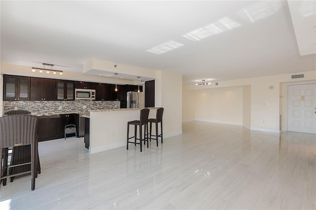 kitchen featuring a breakfast bar, decorative light fixtures, backsplash, stainless steel appliances, and dark brown cabinets