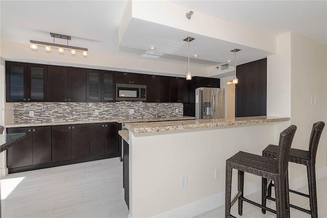 kitchen featuring a kitchen bar, decorative backsplash, kitchen peninsula, stainless steel appliances, and dark brown cabinets