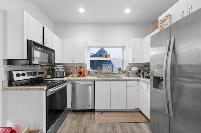 kitchen with light stone countertops, light hardwood / wood-style floors, stainless steel appliances, sink, and white cabinetry