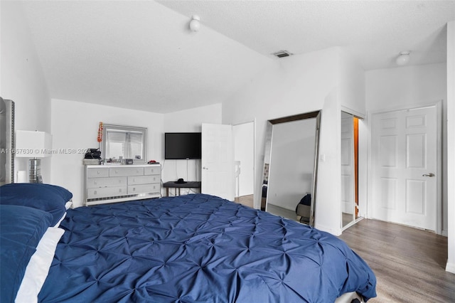 bedroom with lofted ceiling, wood-type flooring, and a textured ceiling