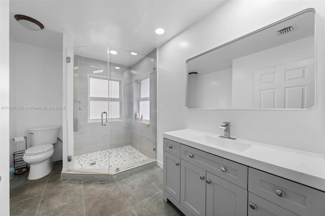 bathroom with a shower with door, vanity, toilet, and tile patterned flooring