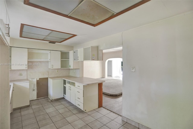 kitchen with light tile patterned floors, decorative backsplash, white cabinets, and kitchen peninsula