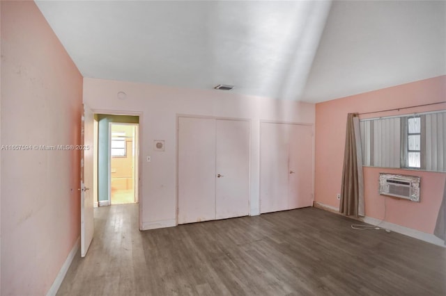 unfurnished bedroom featuring hardwood / wood-style flooring, two closets, and a wall mounted air conditioner