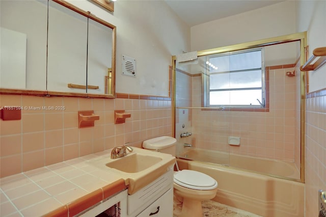 full bathroom with tile walls, tiled shower / bath combo, vanity, and toilet