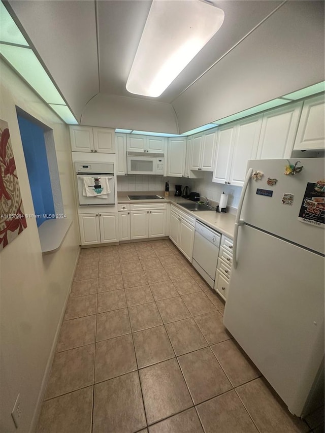 kitchen with white appliances, sink, vaulted ceiling, white cabinets, and light tile patterned floors