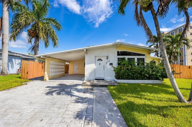 mid-century modern home with fence, decorative driveway, a carport, brick siding, and a front yard