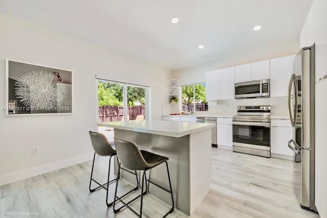 kitchen with light wood-type flooring, white cabinets, appliances with stainless steel finishes, and a breakfast bar area