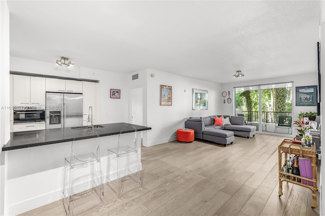 interior space featuring white cabinets, sink, oven, stainless steel fridge with ice dispenser, and light hardwood / wood-style floors