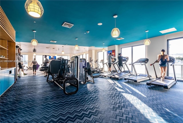 exercise room with plenty of natural light and dark colored carpet