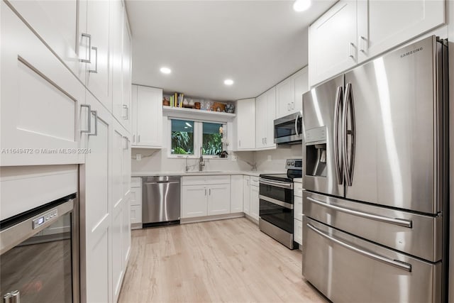 kitchen with light wood-type flooring, white cabinetry, beverage cooler, sink, and appliances with stainless steel finishes