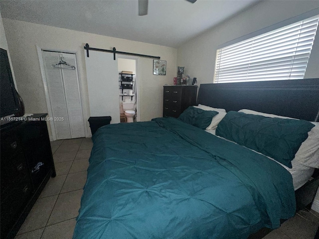 tiled bedroom with ceiling fan, ensuite bath, and a barn door