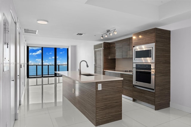 kitchen with a center island with sink, appliances with stainless steel finishes, sink, a water view, and light tile patterned flooring