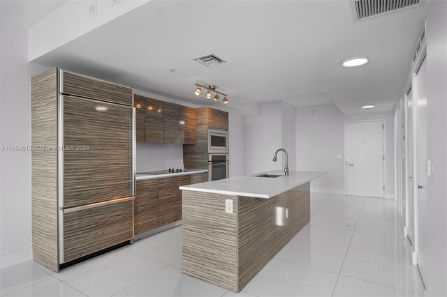 kitchen with a kitchen island with sink, light tile patterned floors, stainless steel appliances, and sink