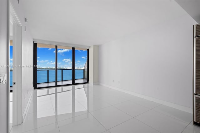 tiled spare room featuring a wall of windows, baseboards, and a water view