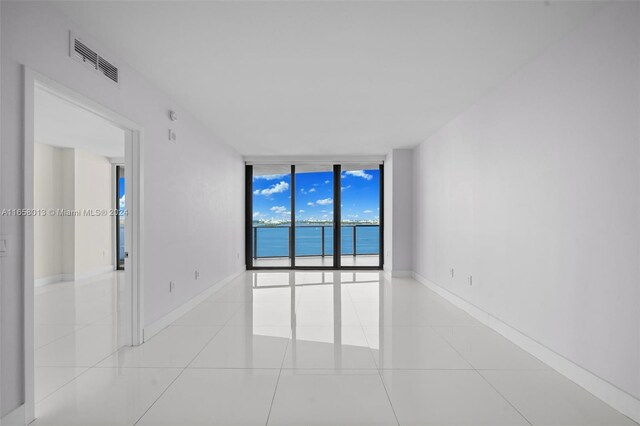 tiled spare room with a wall of windows, visible vents, and baseboards