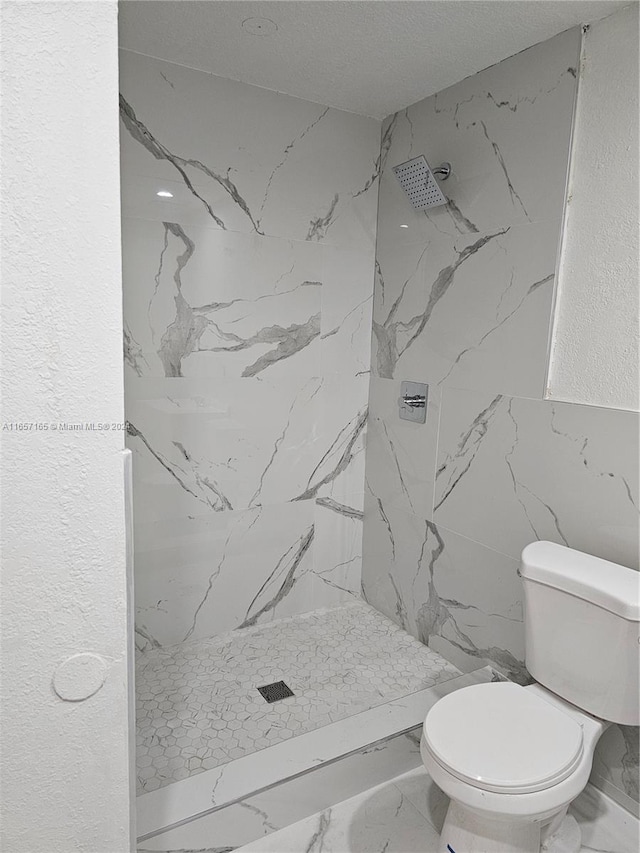 bathroom featuring a textured ceiling, toilet, and tiled shower