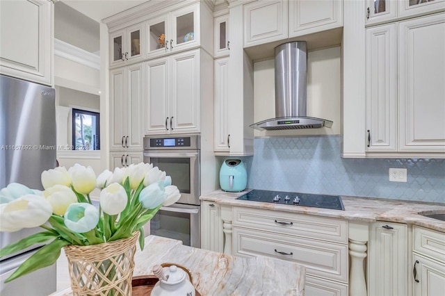 kitchen featuring white cabinets, backsplash, light stone countertops, stainless steel appliances, and wall chimney range hood