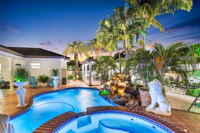 pool at dusk with a patio and an in ground hot tub