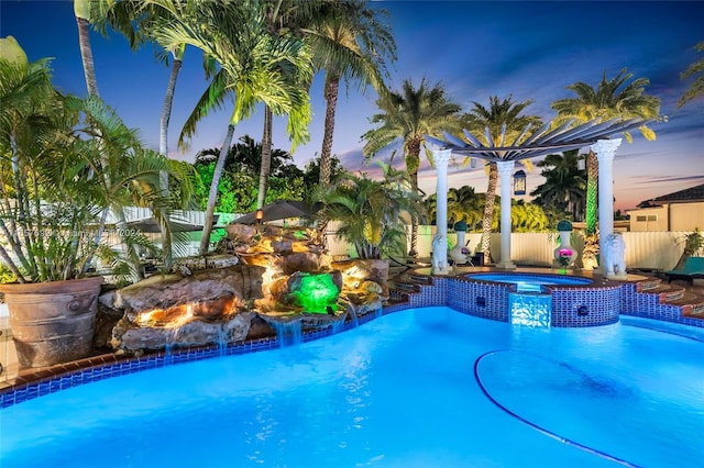 pool at dusk with pool water feature and an in ground hot tub