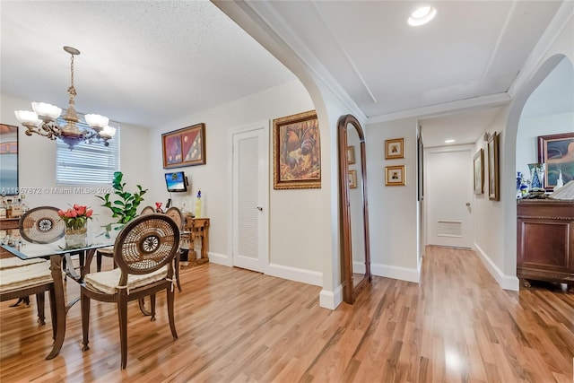 dining space with a textured ceiling, a notable chandelier, and light hardwood / wood-style floors