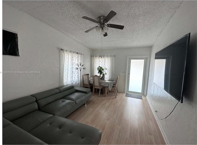 living room featuring light wood-type flooring, ceiling fan, and a textured ceiling