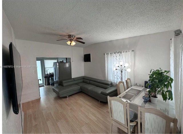 living room featuring ceiling fan with notable chandelier, a textured ceiling, and light hardwood / wood-style flooring