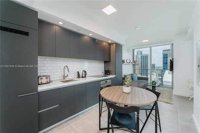 kitchen with tasteful backsplash, sink, a wall of windows, black electric stovetop, and light tile patterned floors