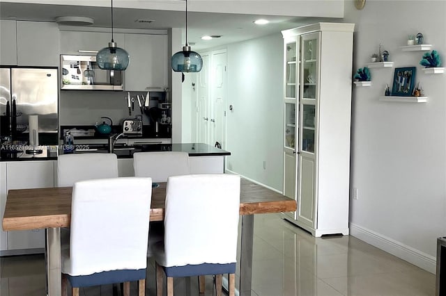 kitchen featuring white cabinets, dark countertops, glass insert cabinets, hanging light fixtures, and stainless steel appliances