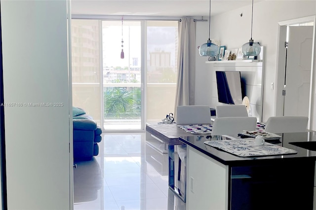 kitchen with a wall of windows, dark countertops, hanging light fixtures, and light tile patterned floors