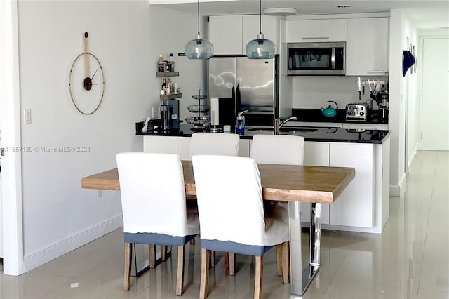 kitchen with pendant lighting, stainless steel appliances, white cabinetry, and light tile patterned flooring