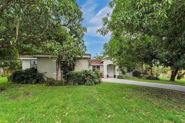 view of front of home featuring a front yard, fence, driveway, stucco siding, and a tiled roof