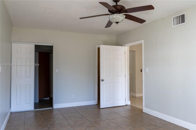 unfurnished bedroom with ceiling fan, a closet, a textured ceiling, and tile patterned flooring