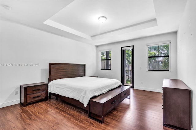 bedroom featuring a raised ceiling, dark hardwood / wood-style floors, and access to exterior