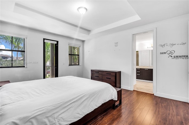 bedroom featuring ensuite bathroom, a raised ceiling, and dark wood-type flooring