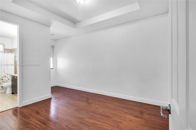 unfurnished bedroom with a tray ceiling, connected bathroom, and dark hardwood / wood-style flooring