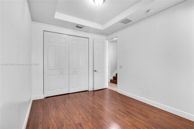 unfurnished bedroom with dark wood-type flooring, a closet, and a raised ceiling