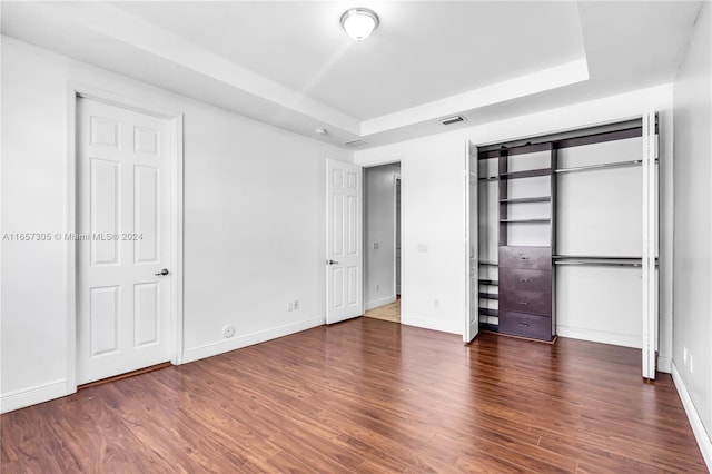 unfurnished bedroom with a tray ceiling and dark hardwood / wood-style floors