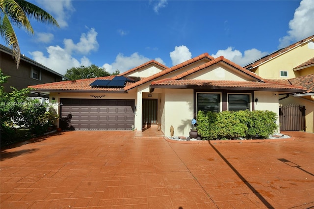 mediterranean / spanish-style home featuring roof mounted solar panels, stucco siding, a tiled roof, and a garage