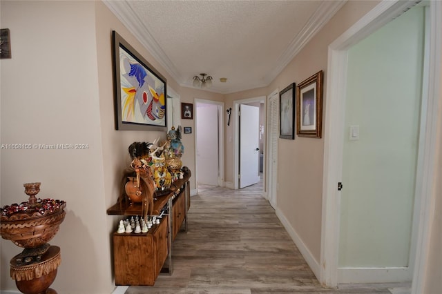 hallway with baseboards, ornamental molding, light wood-type flooring, and a textured ceiling