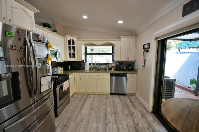 kitchen featuring light wood finished floors, a sink, stainless steel appliances, light stone countertops, and decorative backsplash