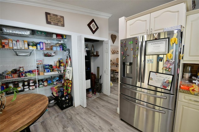 kitchen featuring stainless steel fridge, cream cabinets, light wood-type flooring, a textured ceiling, and ornamental molding