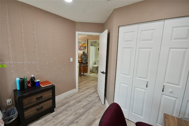 bedroom featuring light wood finished floors, a textured ceiling, baseboards, and a closet