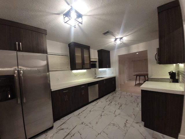 kitchen featuring a textured ceiling, dark brown cabinets, tasteful backsplash, stainless steel appliances, and sink