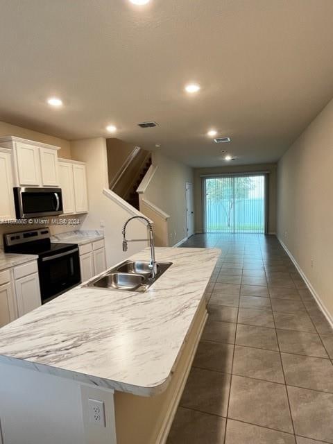 kitchen with dark tile patterned flooring, an island with sink, sink, black range with electric stovetop, and white cabinets