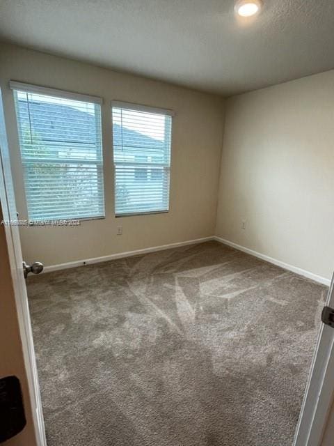 spare room with dark colored carpet, a wealth of natural light, and a textured ceiling