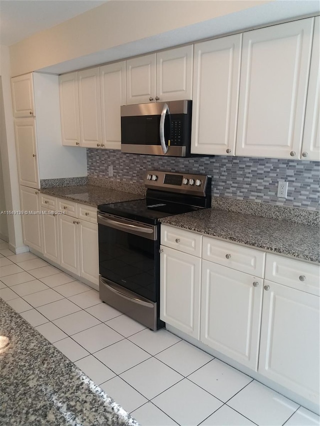 kitchen featuring white cabinets, light tile patterned floors, stainless steel appliances, dark stone counters, and decorative backsplash