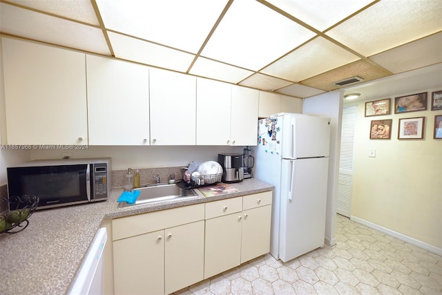 kitchen with white appliances, a drop ceiling, white cabinetry, and sink